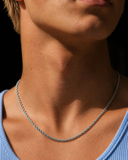 Close-up of a silver chain necklace on a person's neck with a blue shirt.