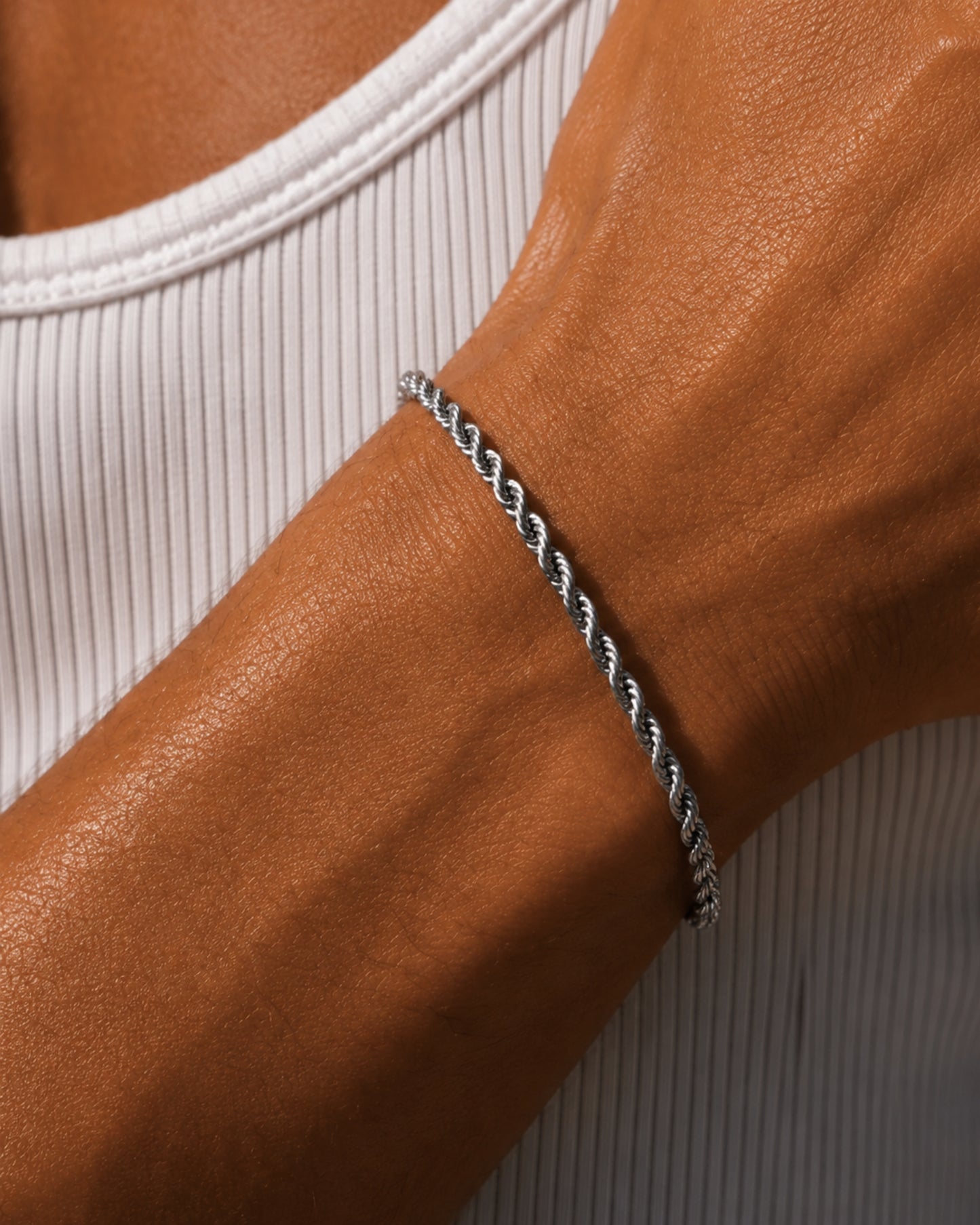 Close-up of a twisted silver bracelet on a tanned wrist wearing a white ribbed tank top.