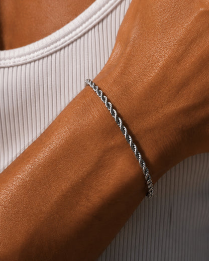 Close-up of a twisted silver bracelet on a tanned wrist wearing a white ribbed tank top.
