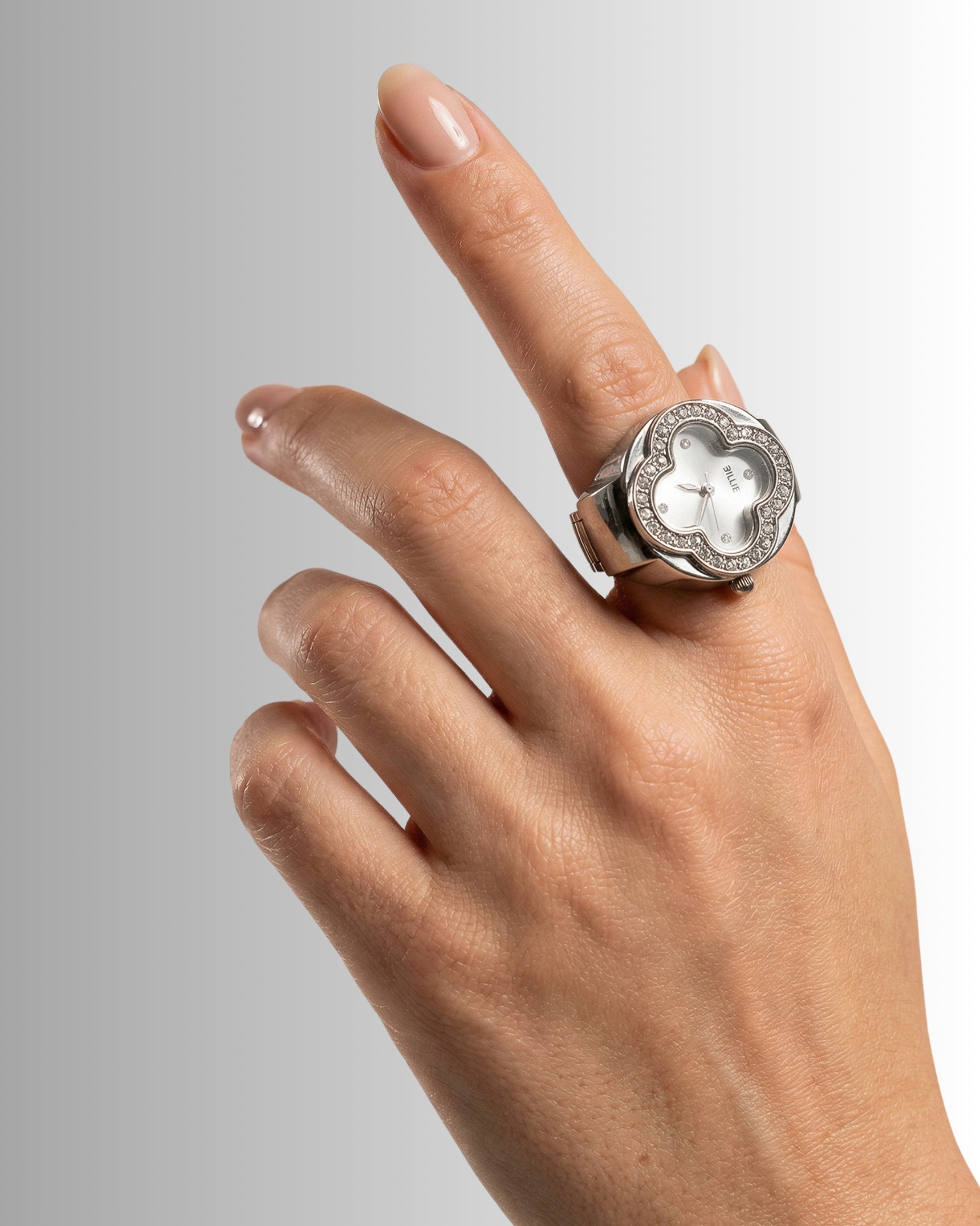 Hand with a silver ring featuring a round watch face and decorative stones.