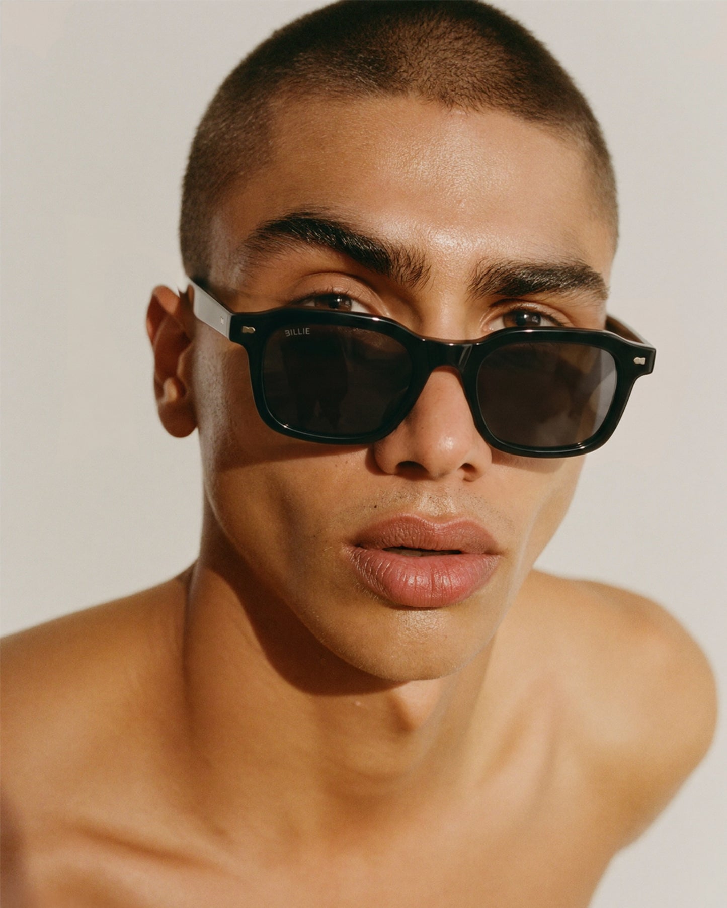 Close-up of a person wearing black sunglasses with a light background.