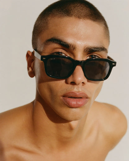 Close-up of a person wearing black sunglasses with a light background.