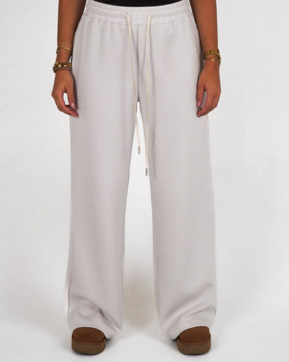 Person wearing light-colored wide-leg pants and brown shoes, standing on a plain background.