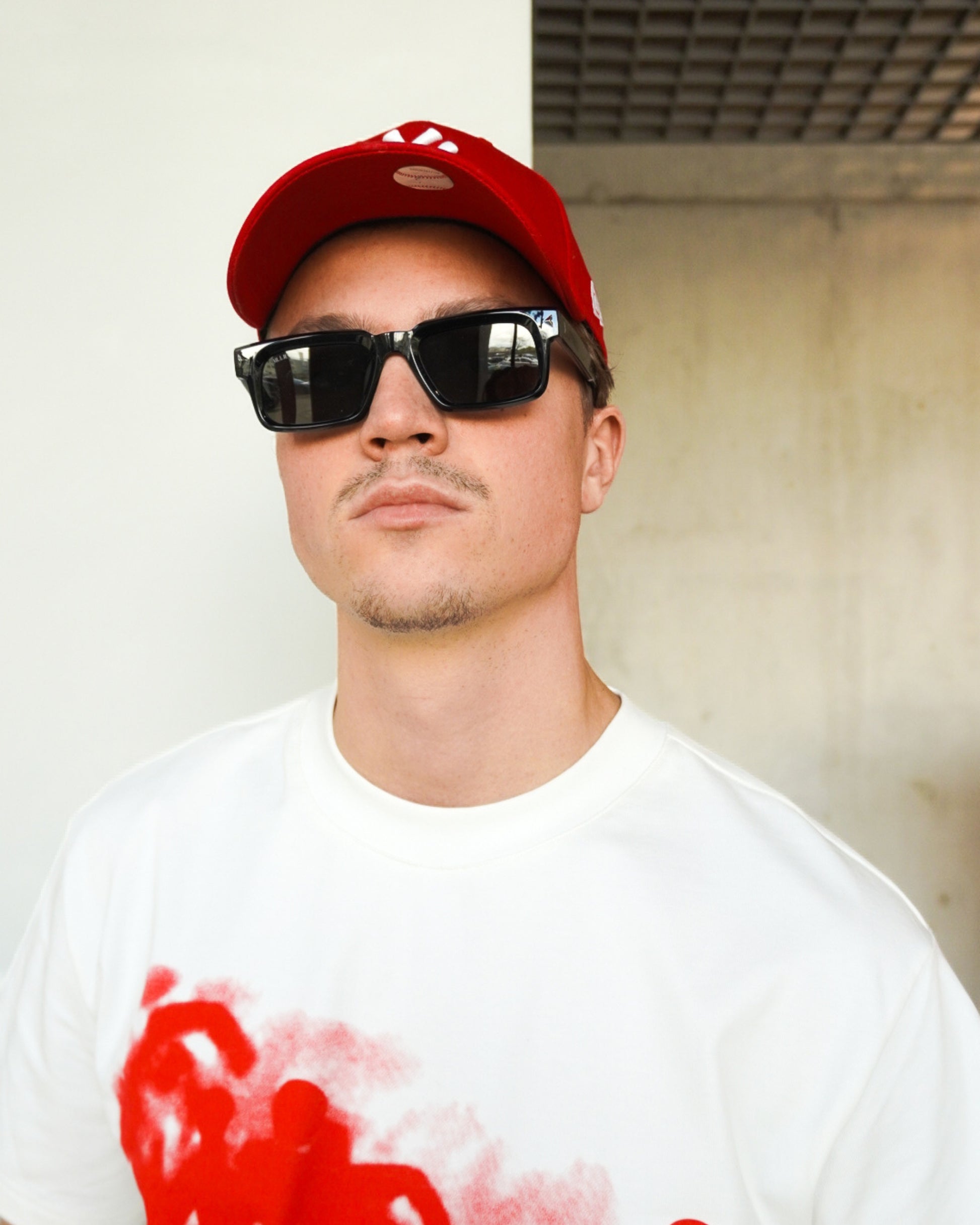 Person wearing a red cap and sunglasses, with a white shirt featuring red graphic design.
