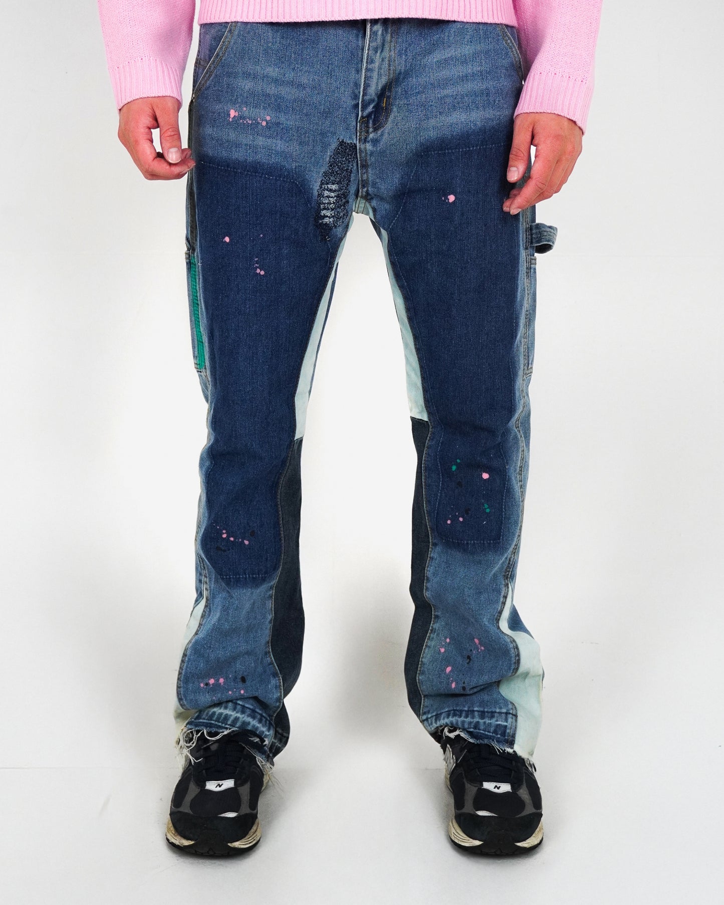 Person wearing distressed blue jeans with colorful paint splatters and black sneakers.