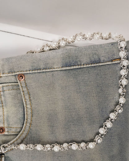 Close-up of a denim pocket with a pearl and silver chain detail.
