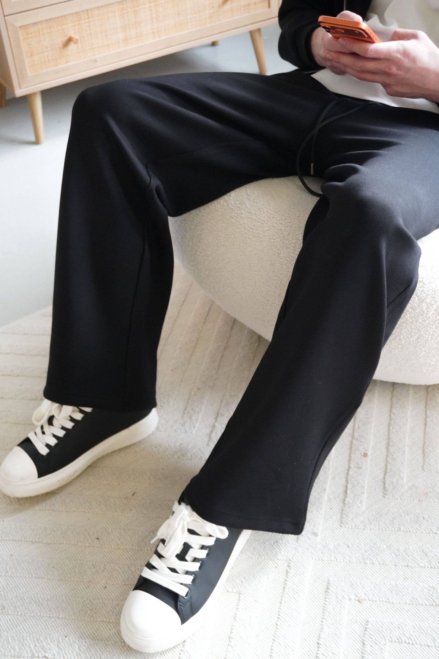 Person wearing black pants and white sneakers sitting on a couch.