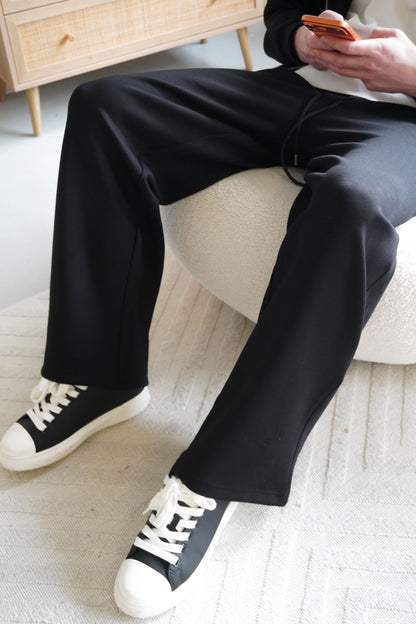 Person wearing black pants and white sneakers sitting on a couch.