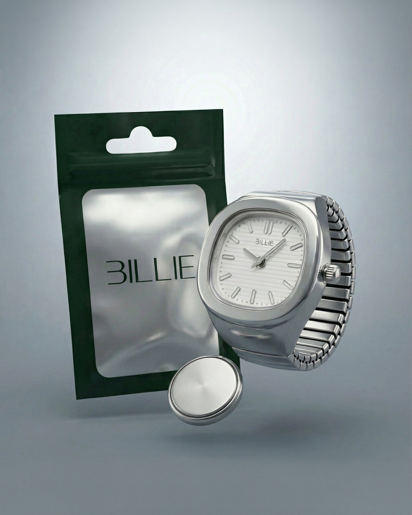 Silver watch with a white face next to a green packaging and a round silver object.