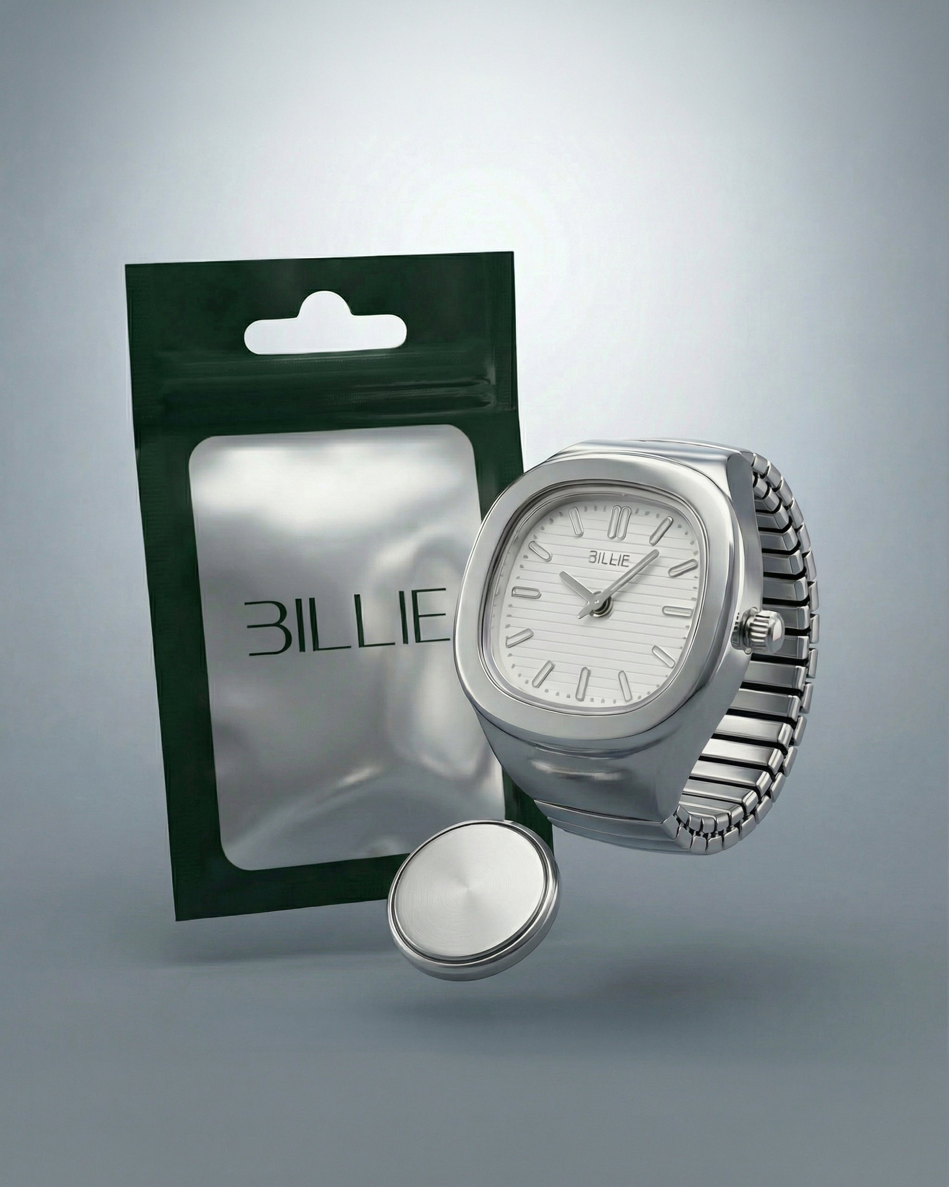 Silver watch with a white face next to a green packaging and a round silver object.