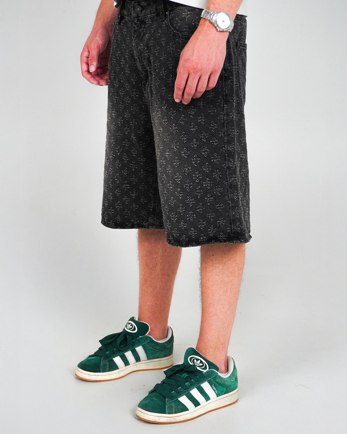 Person wearing patterned black shorts and green sneakers, standing on a plain background.