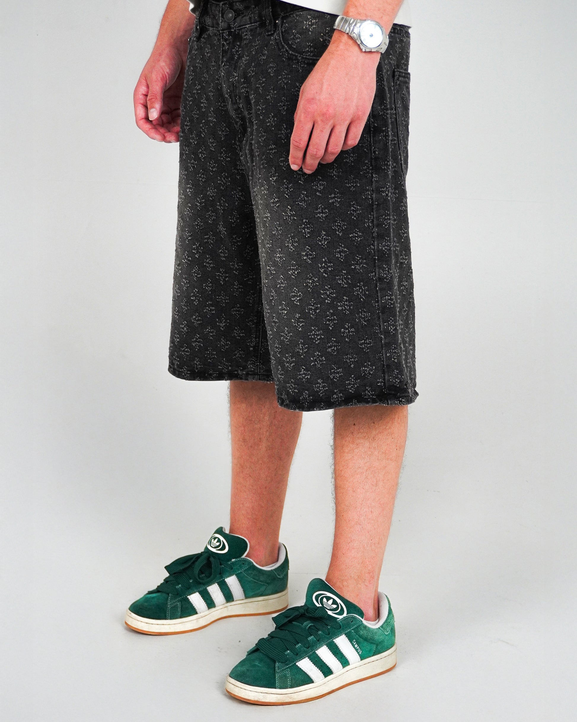 Person wearing patterned black shorts and green sneakers, standing on a plain background.