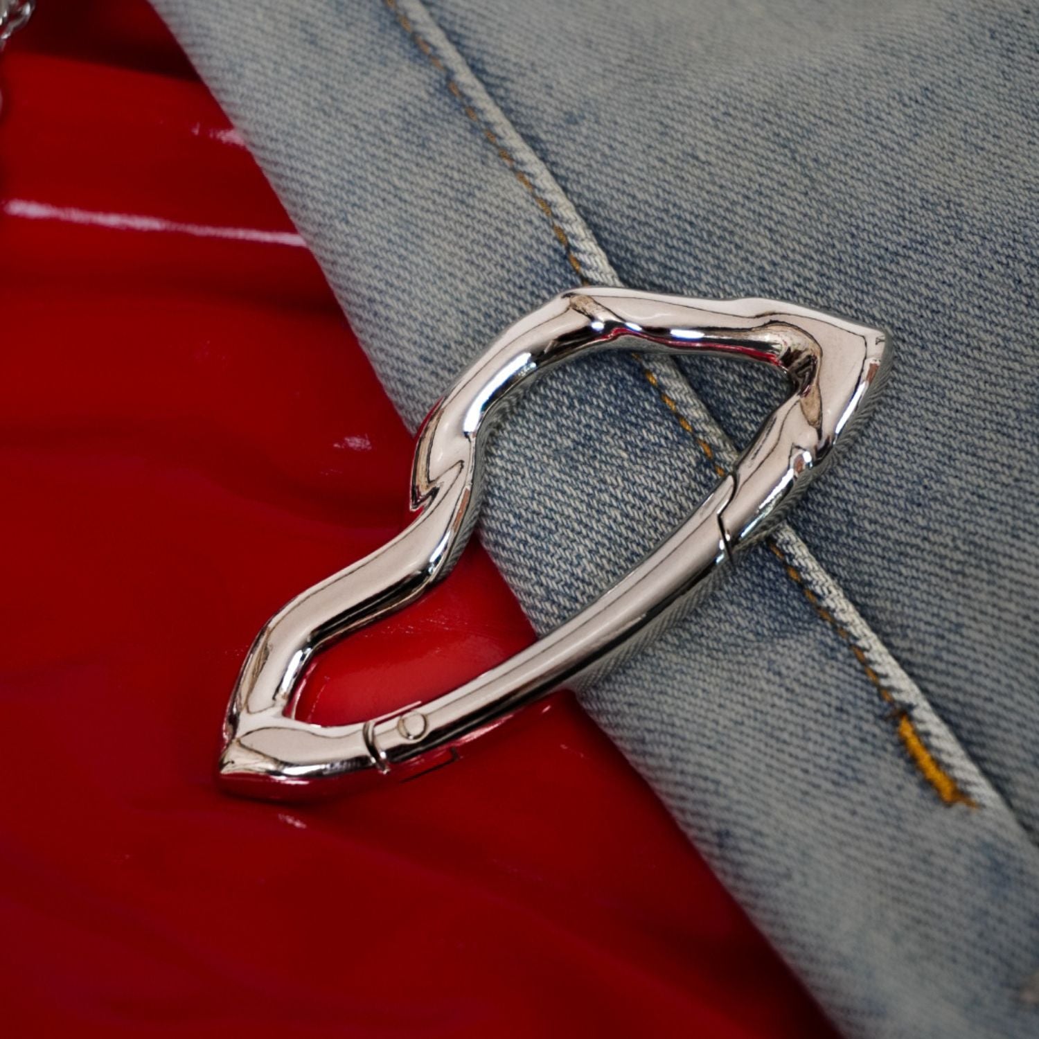 Metallic carabiner attached to a red bag with denim fabric background