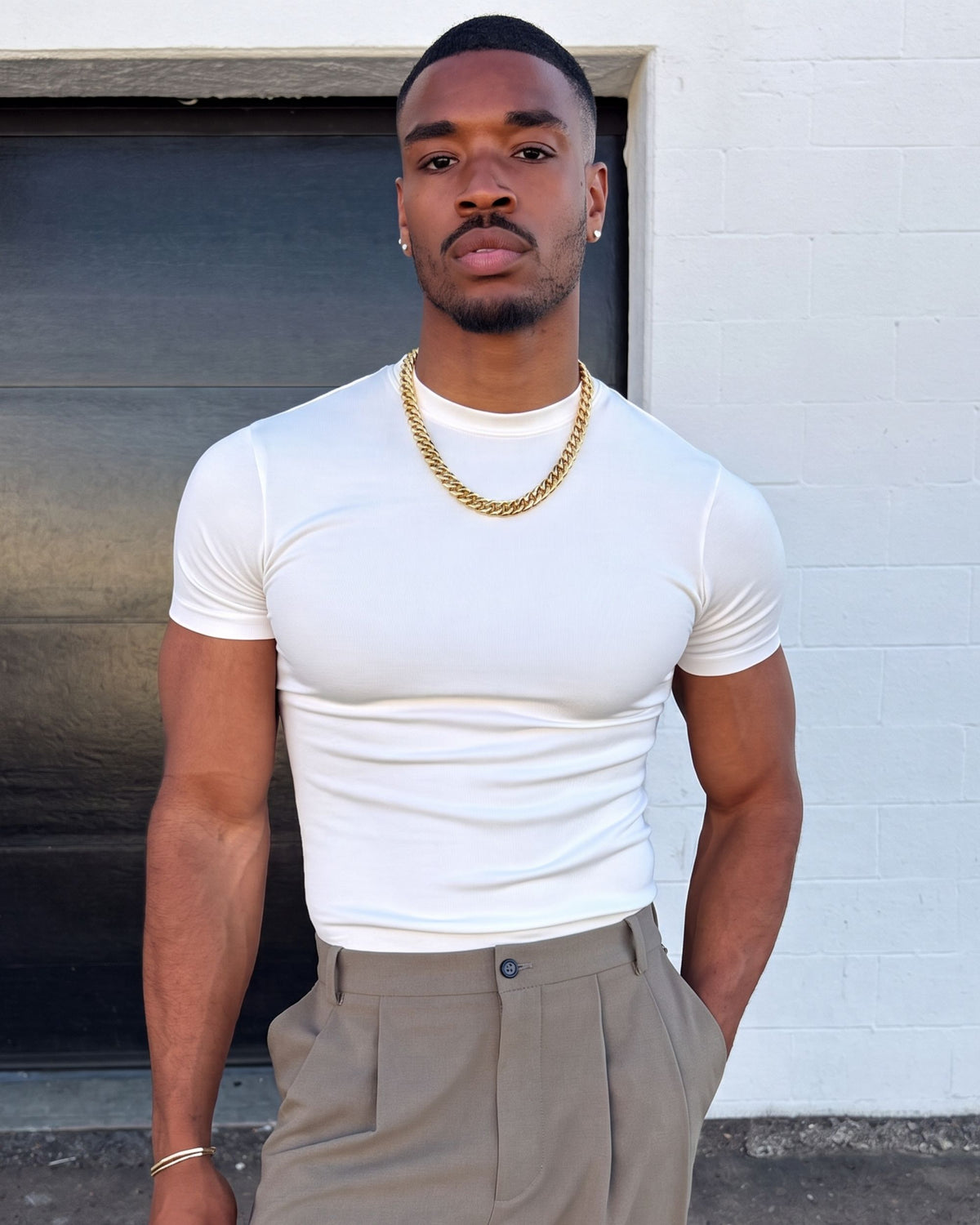 Man in a white T-shirt and beige trousers wearing the gold Billie Cuban Chain 12mm in front of a garage door