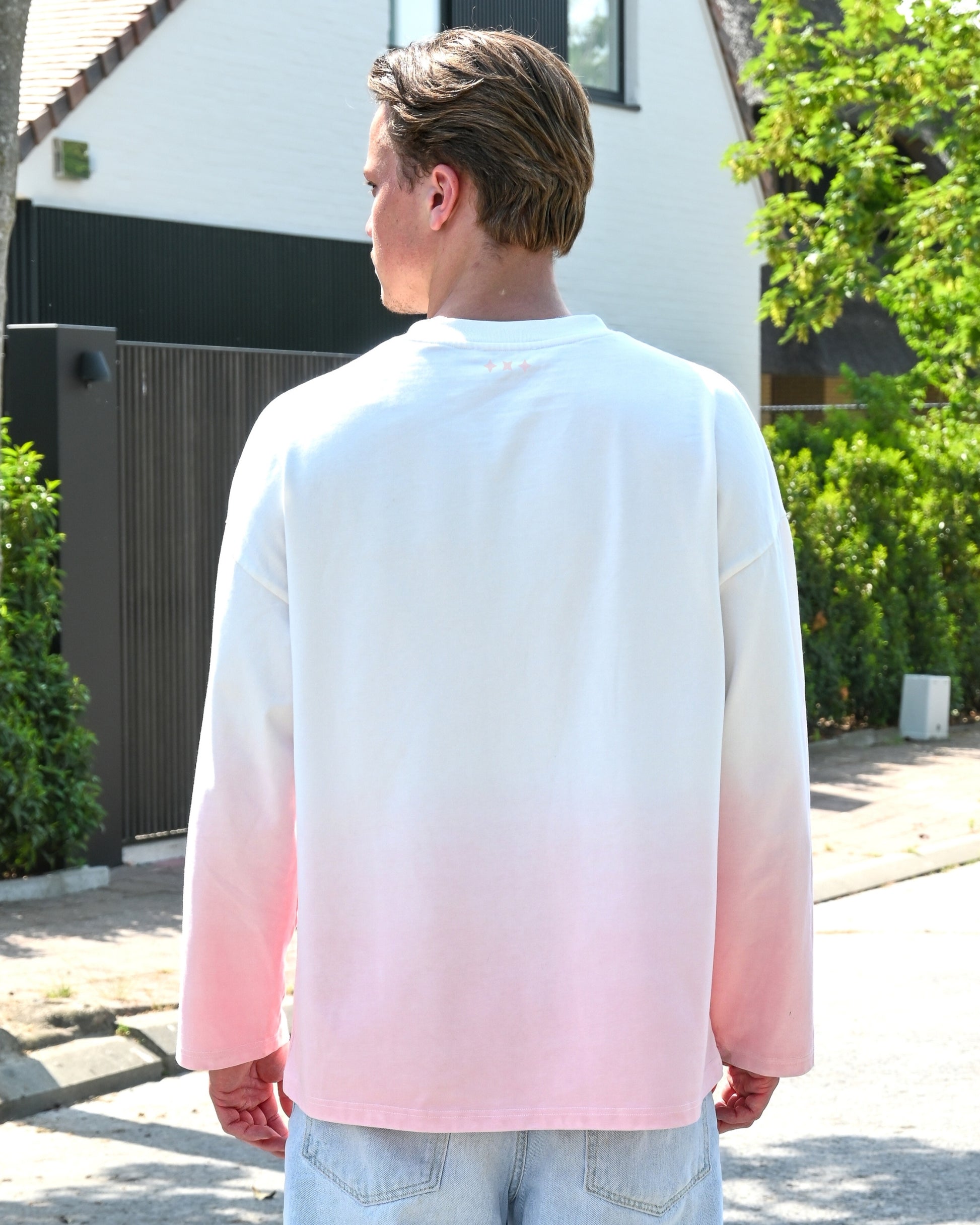 Person wearing a long-sleeve shirt with a gradient from white to pink, viewed from the back.