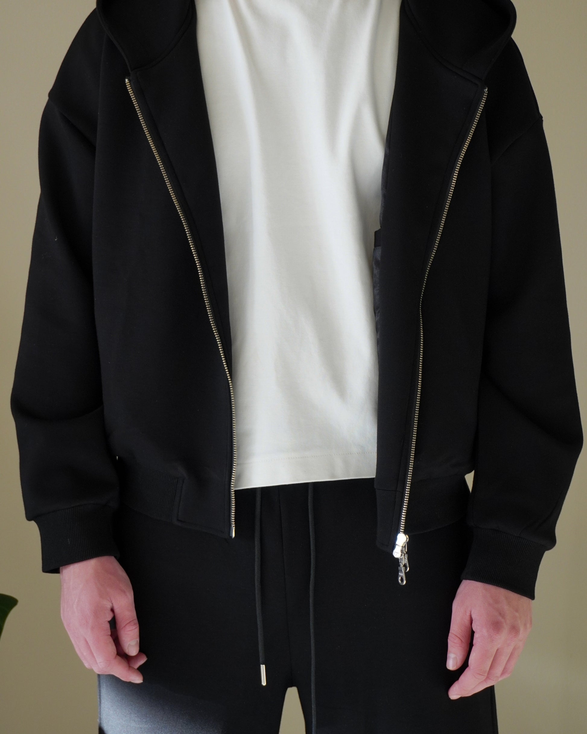 Person wearing a black zip-up hoodie and white t-shirt with black pants.