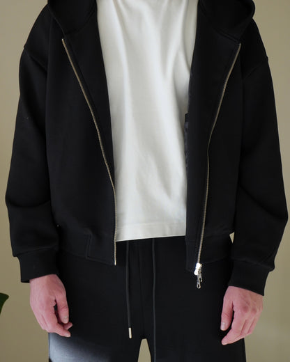 Person wearing a black zip-up hoodie and white t-shirt with black pants.