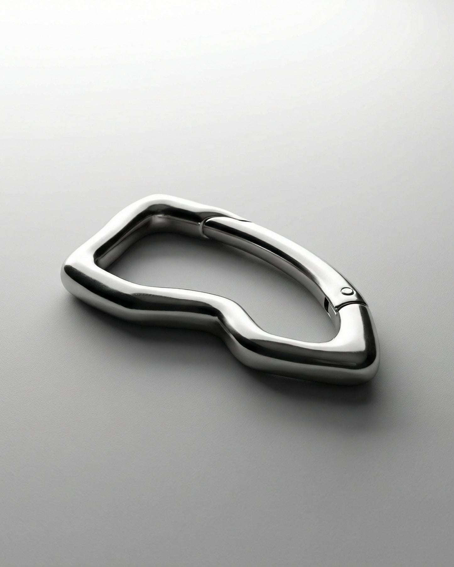 Shiny metallic object with a curved, abstract shape on a light background.