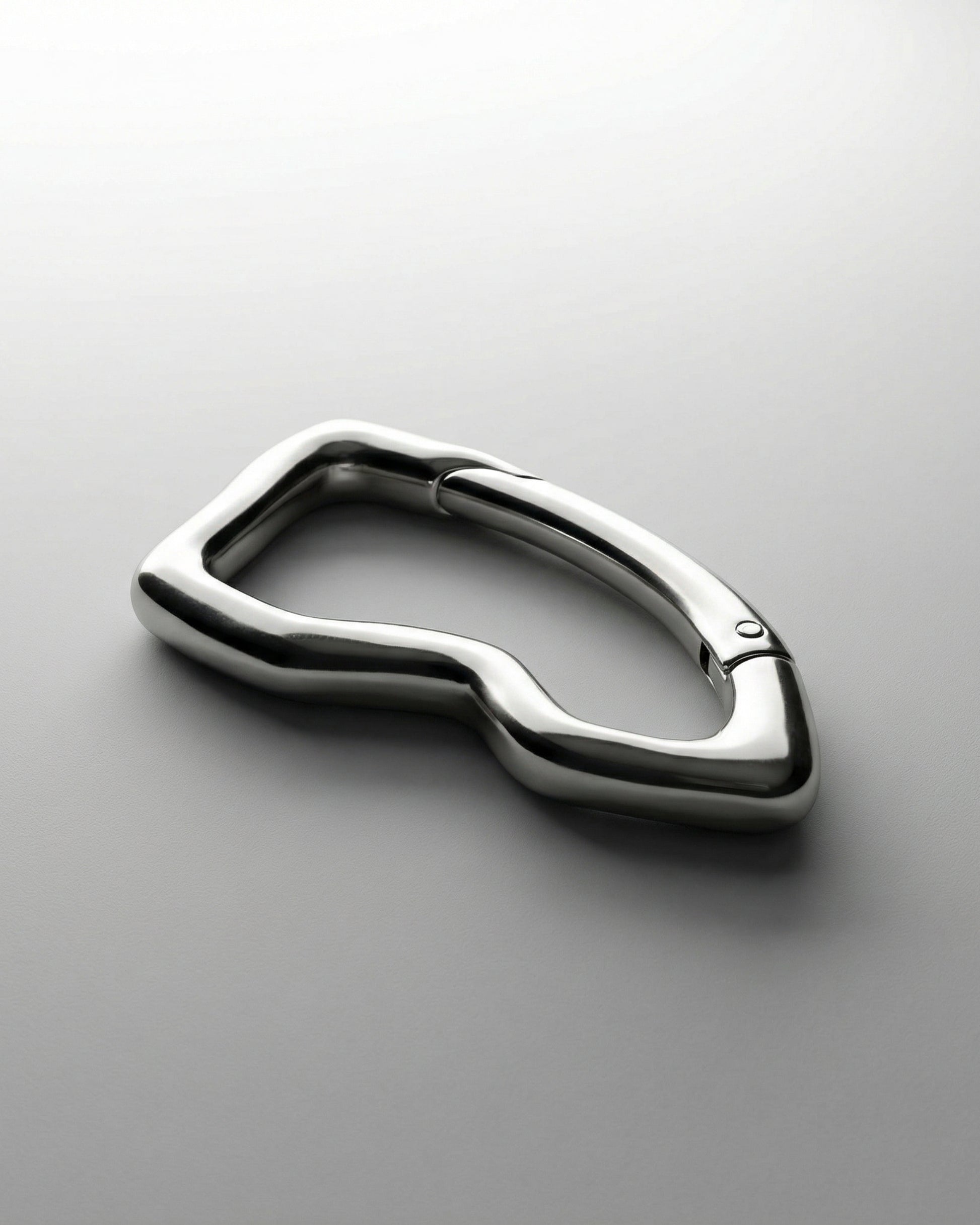 Shiny metallic object with a curved, abstract shape on a light background.