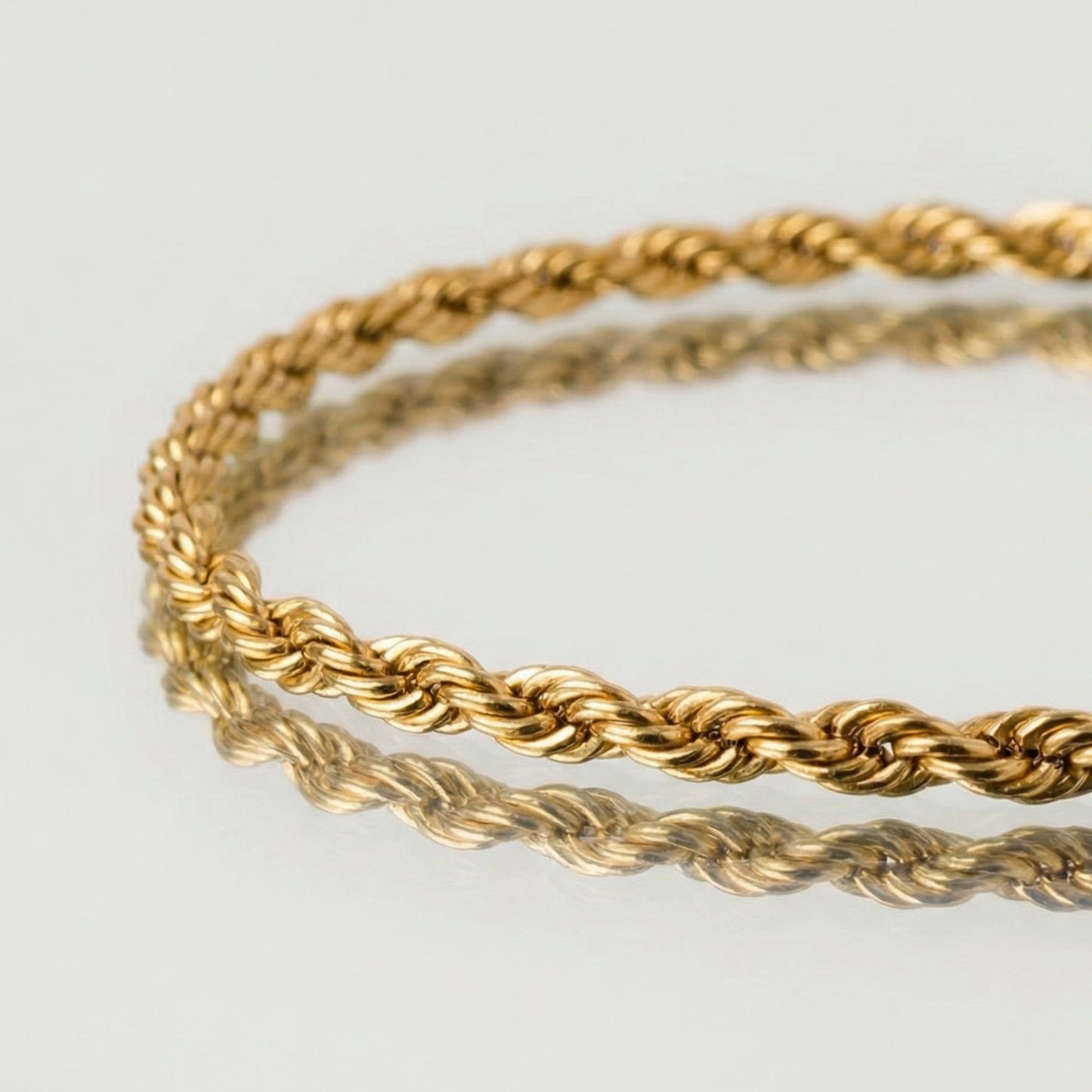 Two gold rope bracelets on a light gray background