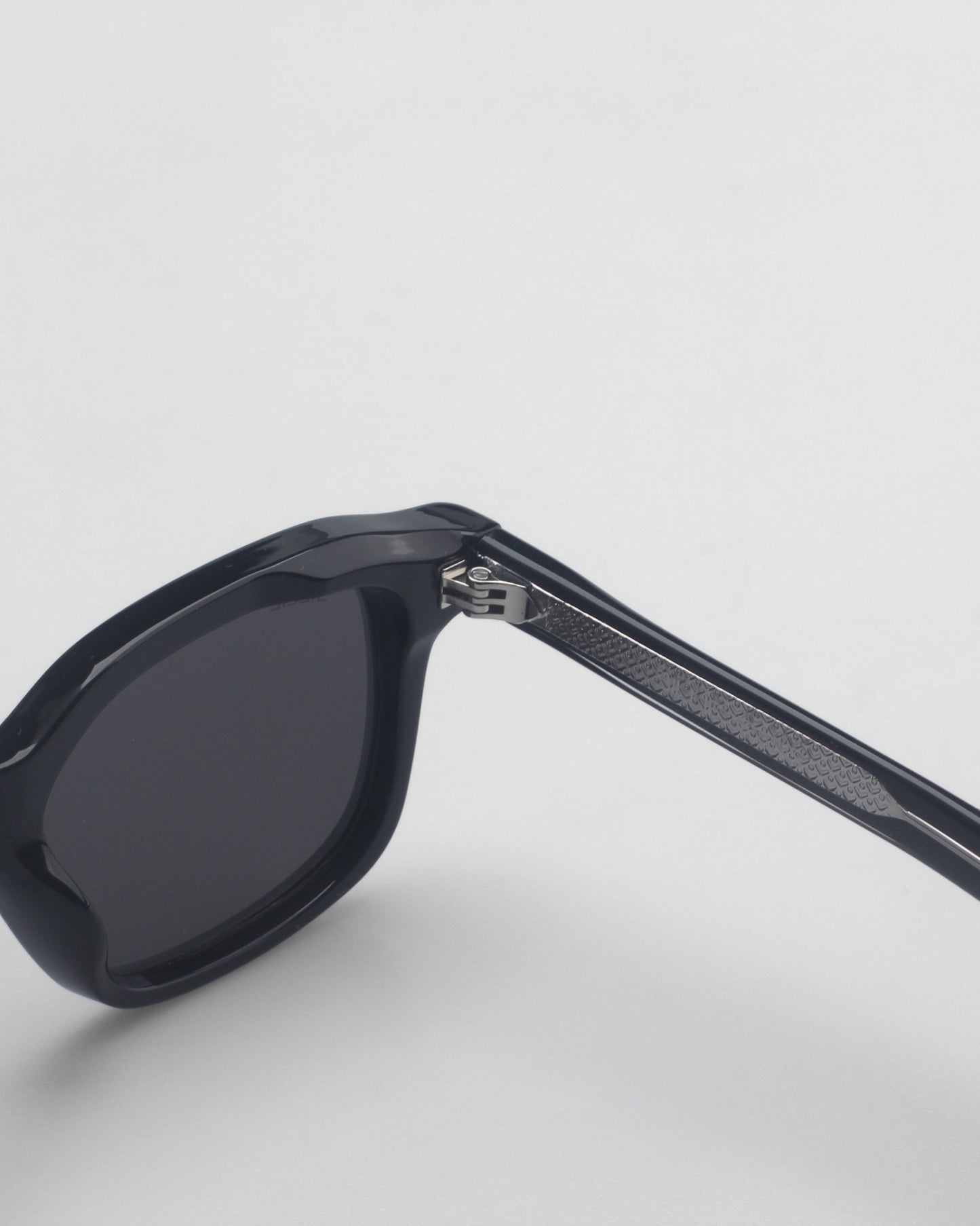 Black sunglasses with a thick frame and patterned temple on a plain background.