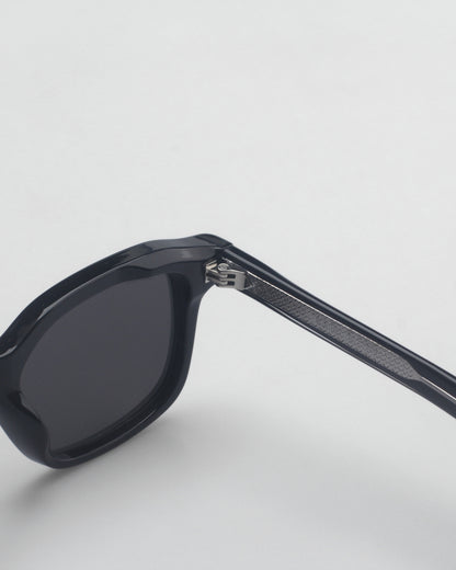 Black sunglasses with a thick frame and patterned temple on a plain background.