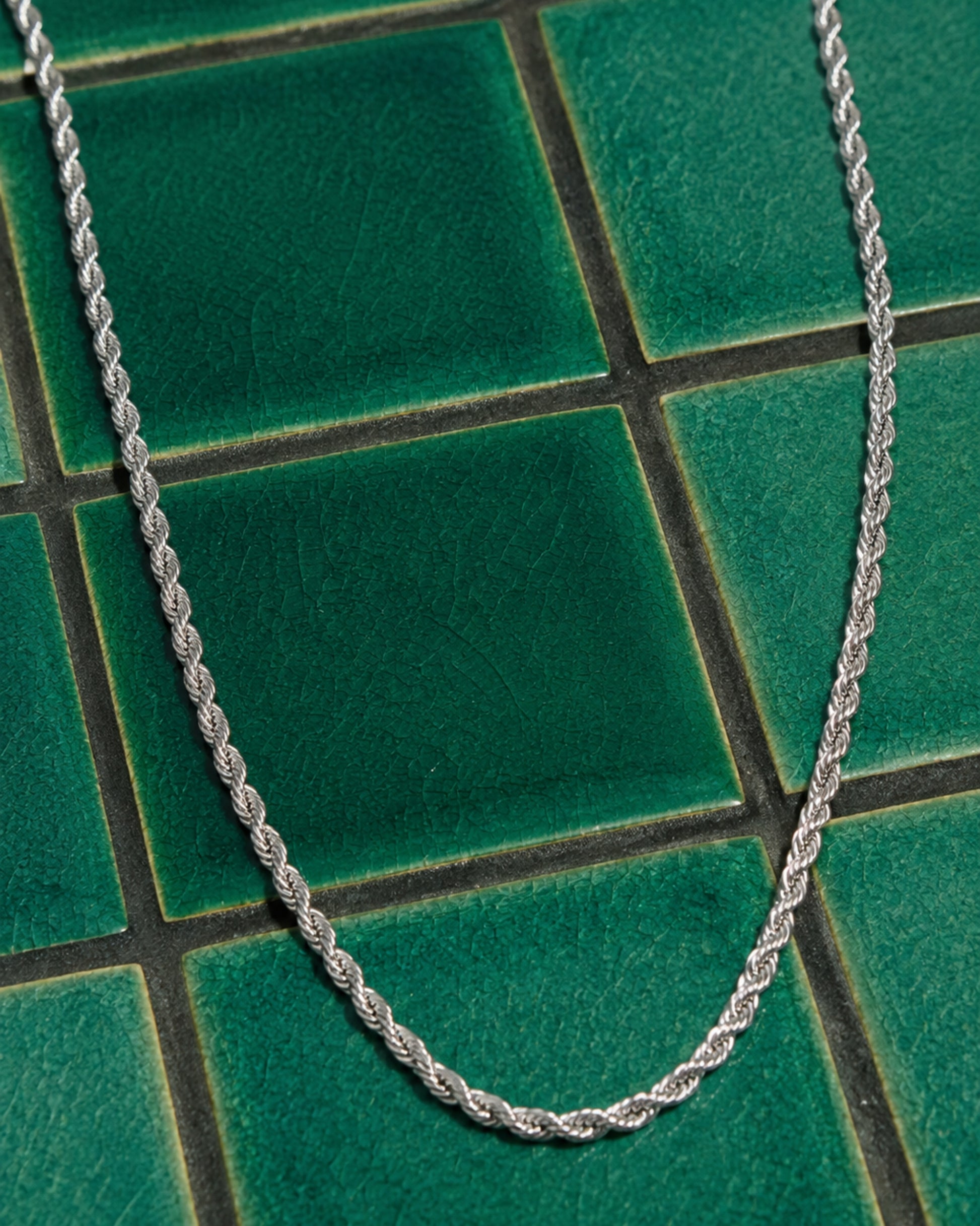 Silver twisted chain necklace on green tiled surface