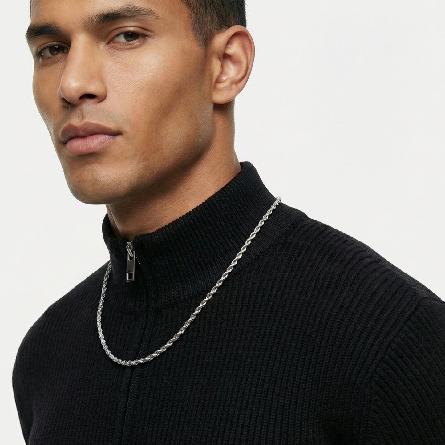 Man wearing a black turtleneck sweater with a silver chain necklace on a plain background