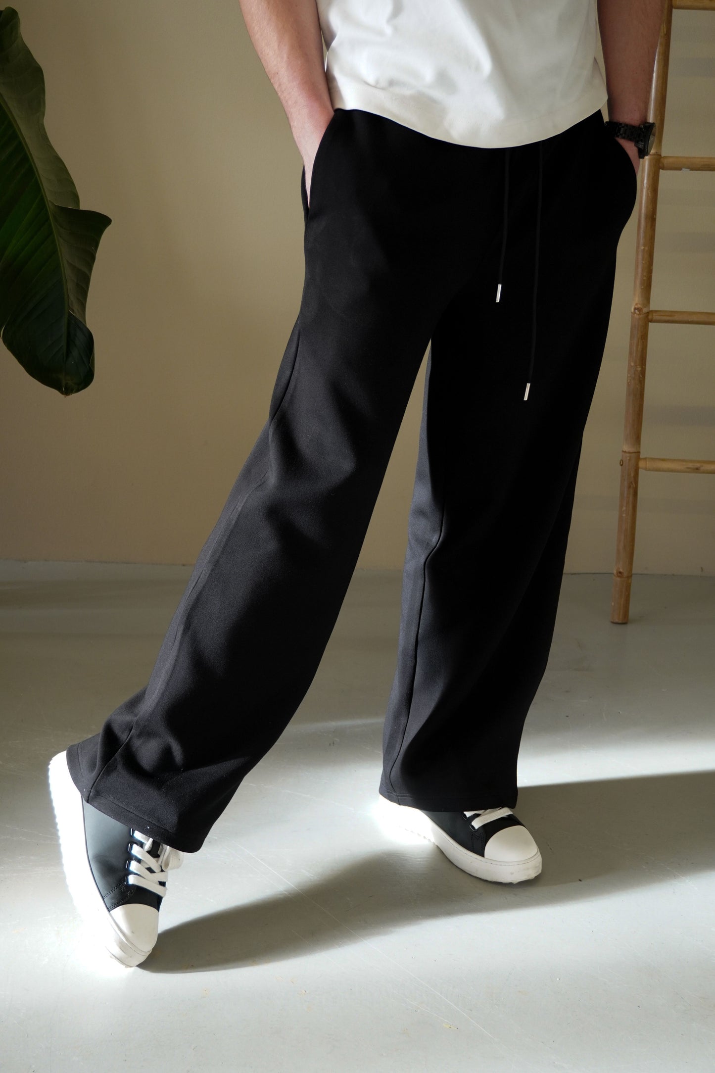 Person wearing black pants and white sneakers in a minimal indoor setting