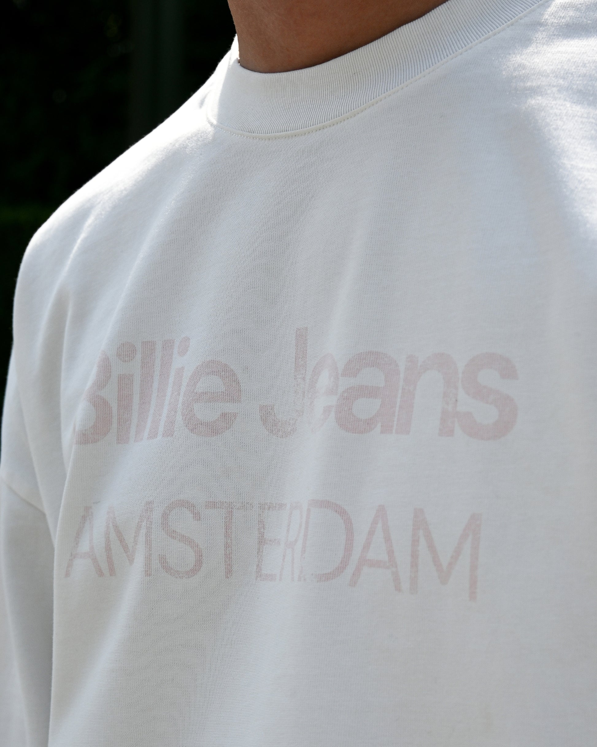 Close-up of a white shirt with faded text reading 'Billie Jeans AMSTERDAM'.