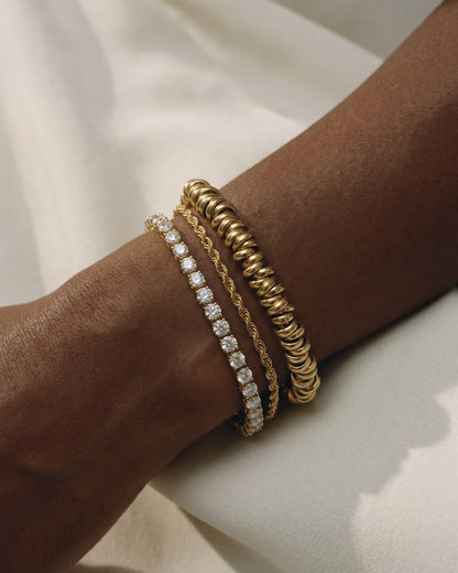 Three gold bracelets on a wrist against a light background.