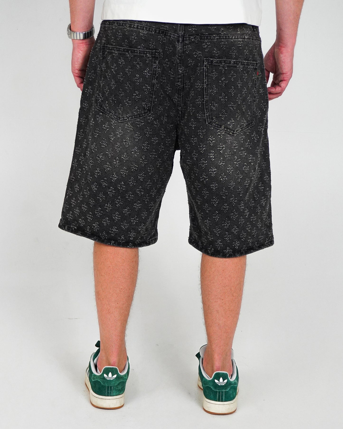 Person wearing black patterned shorts and green sneakers, viewed from the back.
