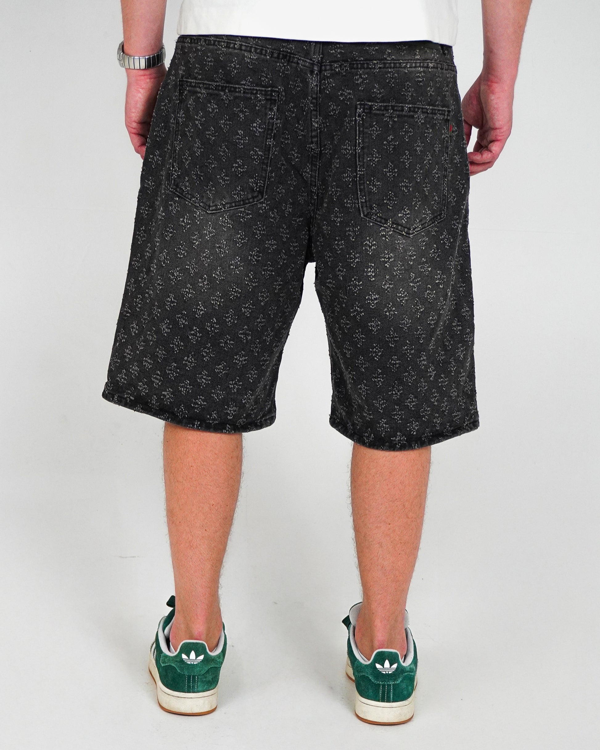 Person wearing black patterned shorts and green sneakers, viewed from the back.