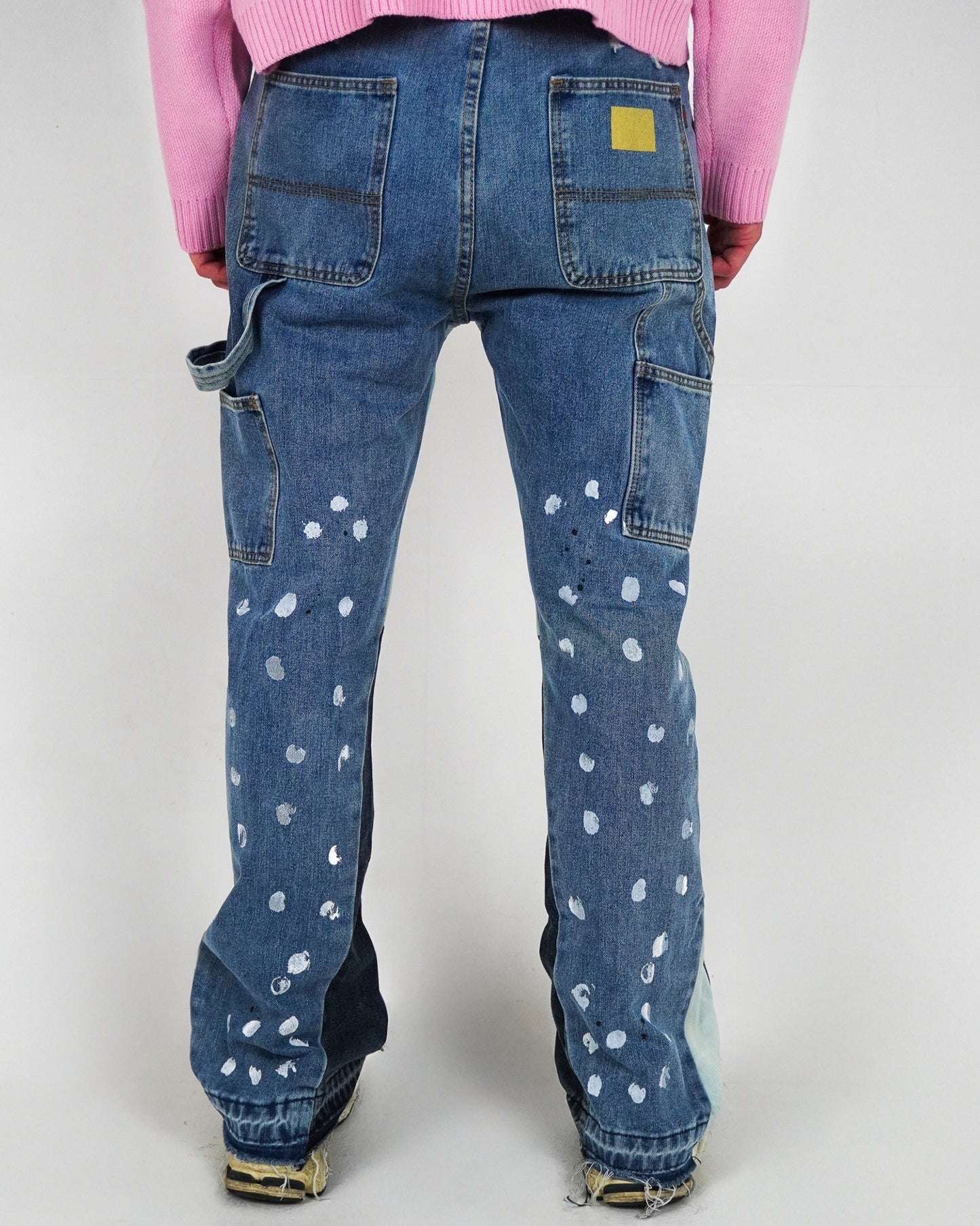 Back view of blue jeans with white paint splatters and a yellow patch.