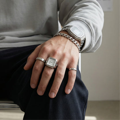 Person wearing multiple silver rings and a watch on a neutral background