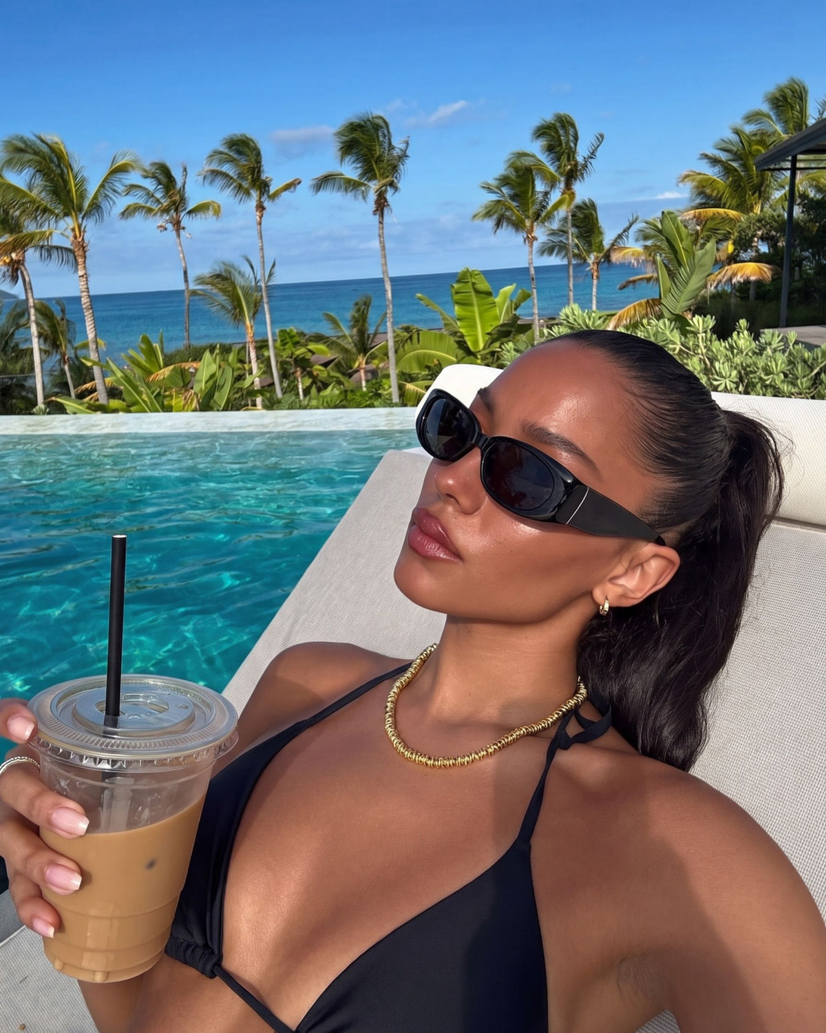 Woman in sunglasses with an iced coffee wearing the gold Billie Spring Chain 7mm by the pool