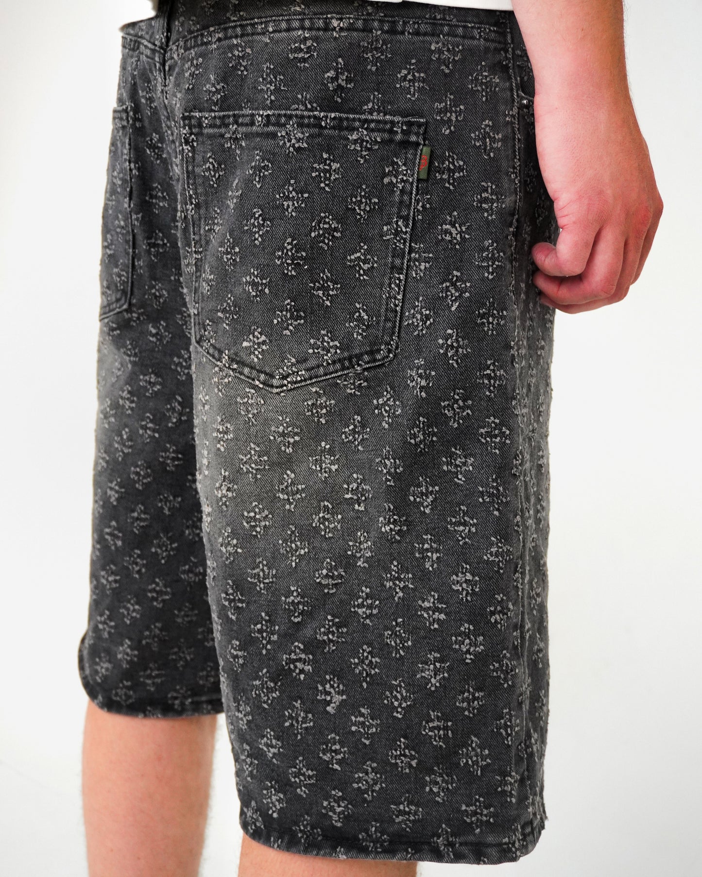 Close-up of patterned shorts with pockets, worn by a person, against a light background.