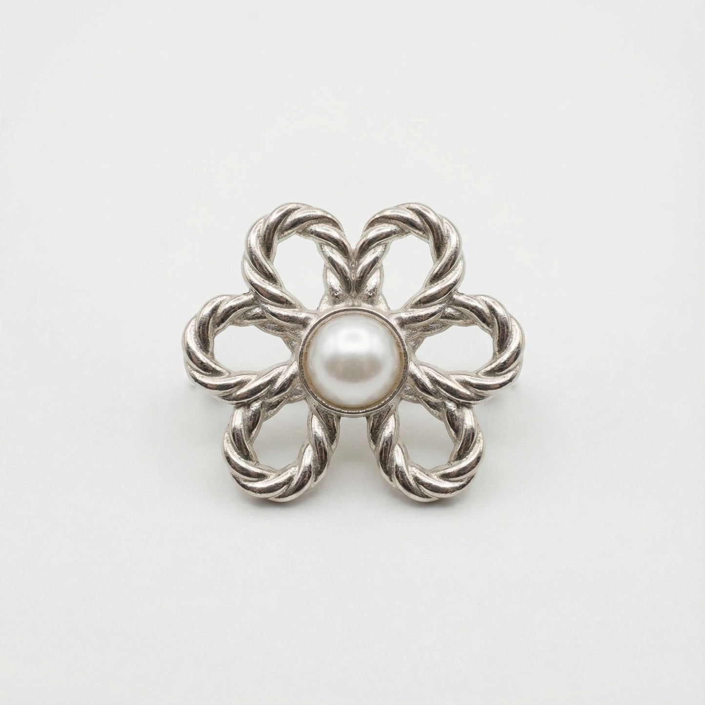 Silver brooch with a central pearl on a white background