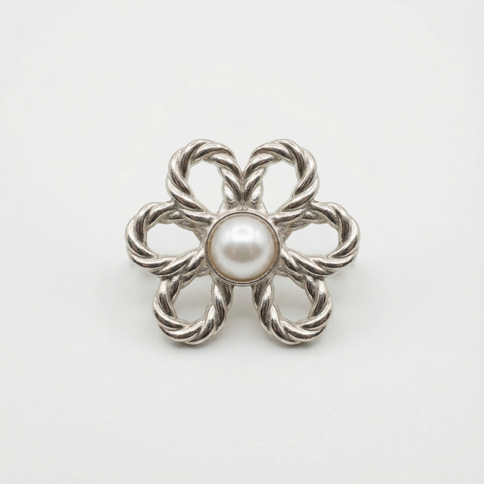 Silver brooch with a central pearl on a white background