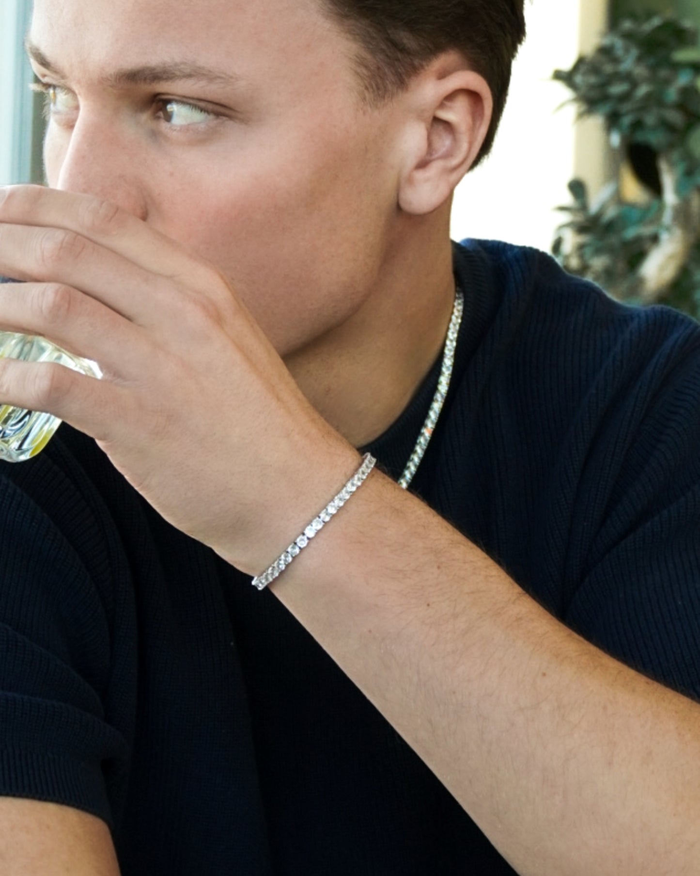 A person holding a glass of water, wearing a silver bracelet and a dark shirt.