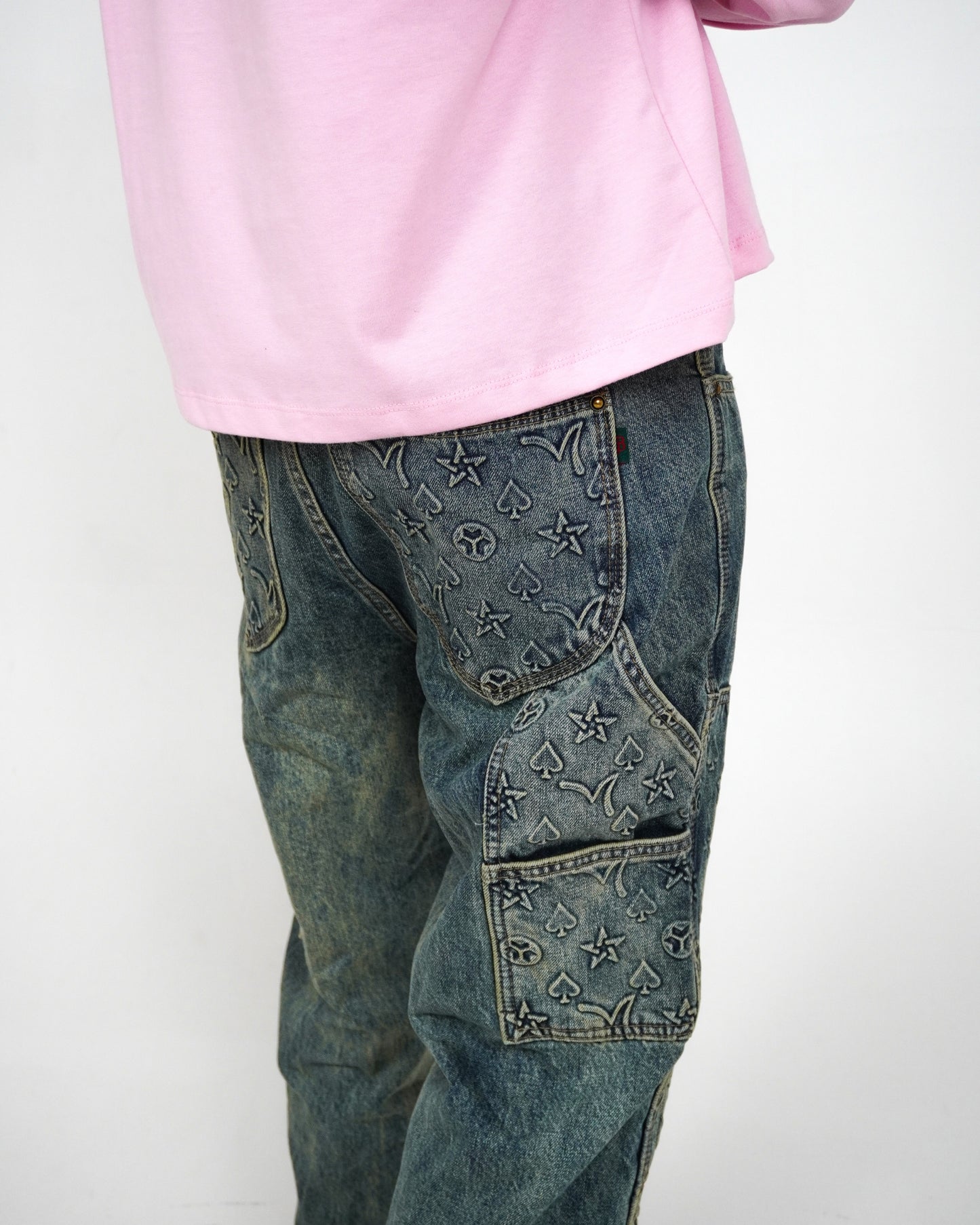 Person wearing a pink long-sleeve shirt and patterned denim jeans.