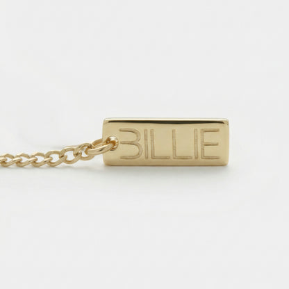 Gold necklace with a rectangular tag engraved with 'BILLIE' on a white background