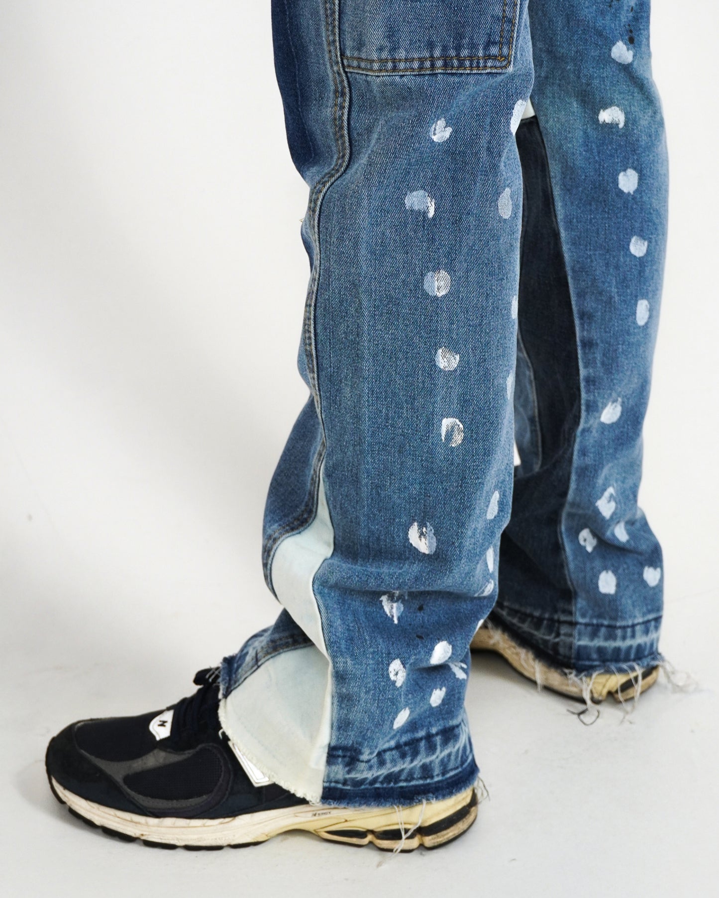 Close-up of jeans with paint splatters and black sneakers.