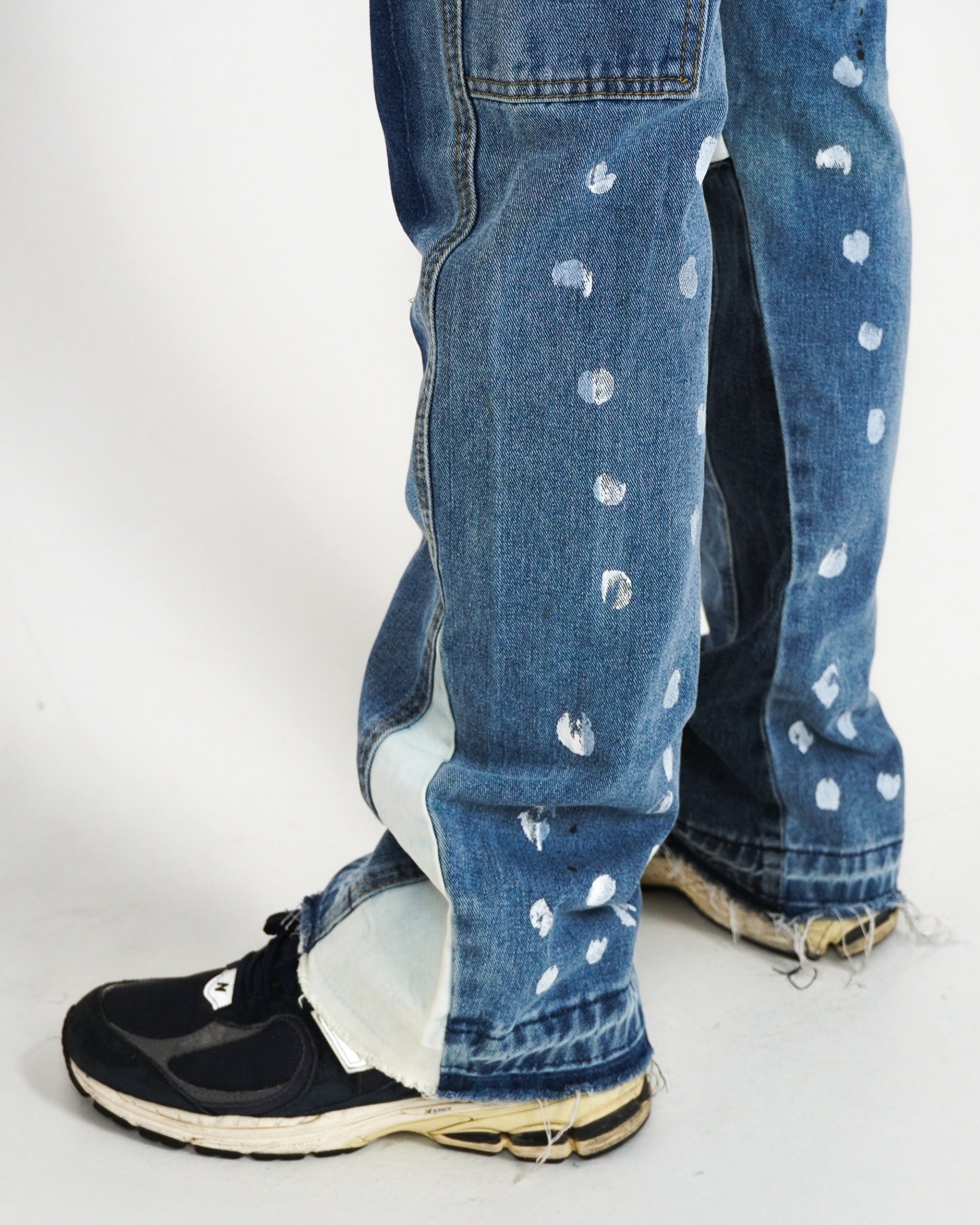 Close-up of jeans with paint splatters and black sneakers.