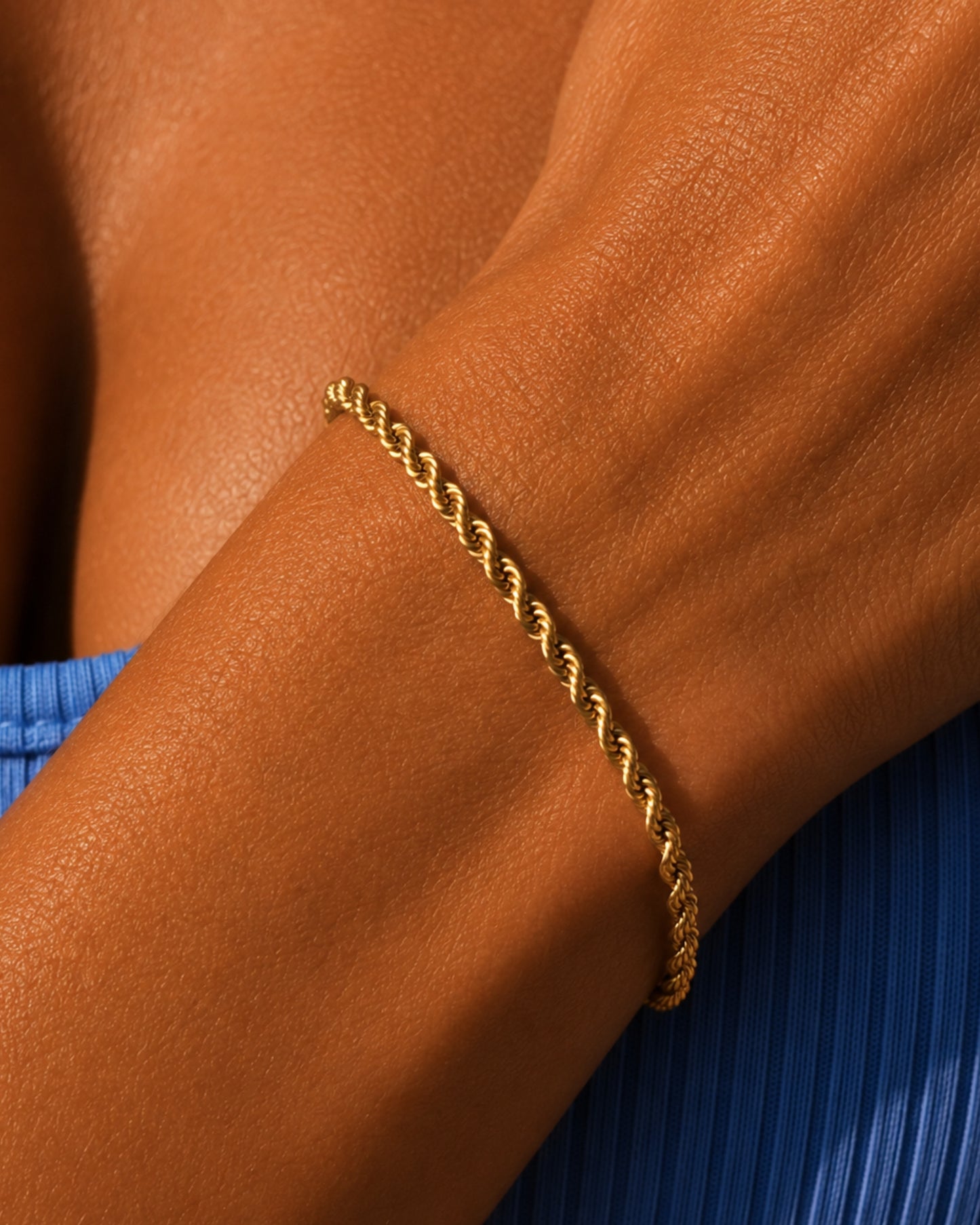 Close-up of a gold twisted bracelet on a tanned arm.