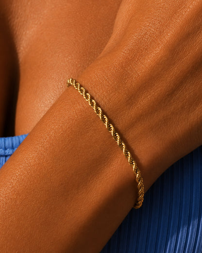 Close-up of a gold twisted bracelet on a tanned arm.