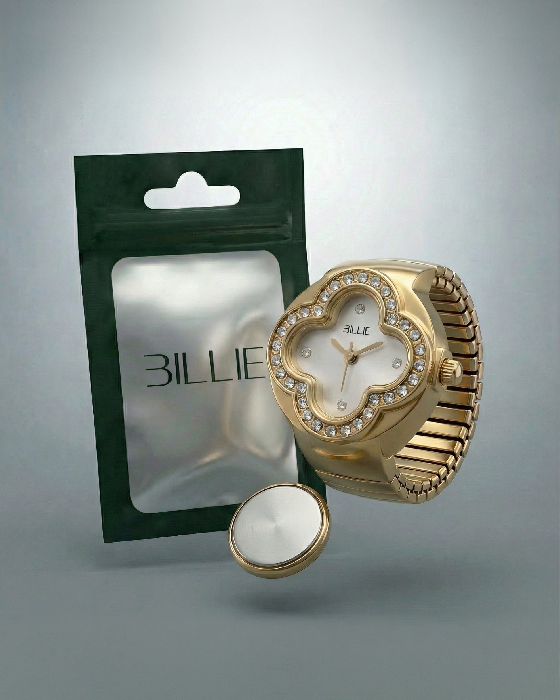 Gold watch with a floral design and crystals, next to a green packaging and a round silver object.