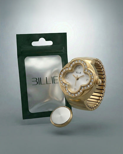 Gold watch with a floral design and crystals, next to a green packaging and a round silver object.