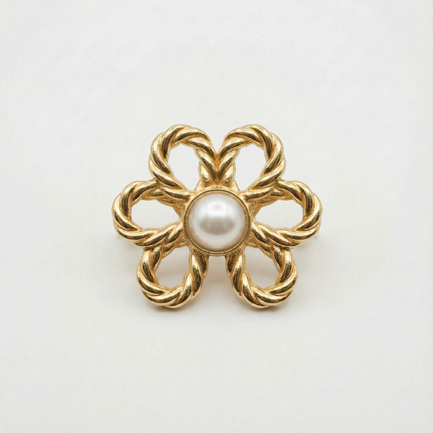 Gold brooch with a central pearl on a white background