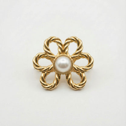 Gold brooch with a central pearl on a white background